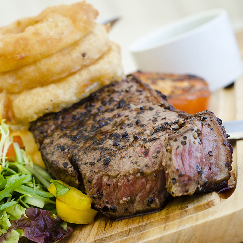 A cooked rump steak with a stack of onion rings and side garnish.