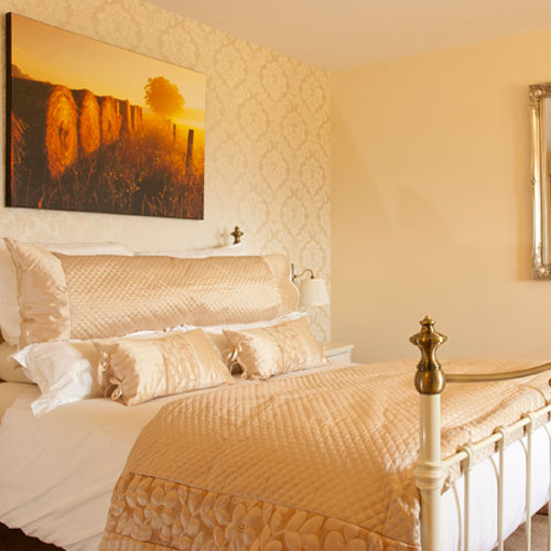 A neatly decorated bed in a room with a painting on the wall of some hay bails.