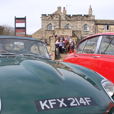 Two vintage jaguar cars with a group of people standing outside the Norfolk Arms in the background.