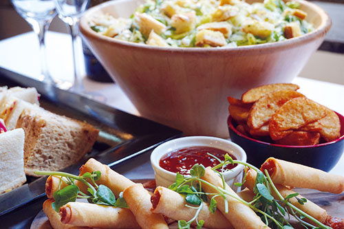A section of a buffet with spring rolls, sandwiches, wedges and salad